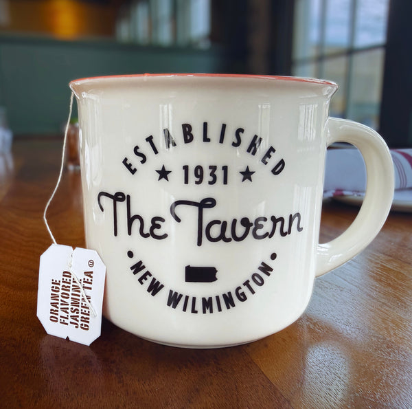 White mug with 'The Tavern' branding and a tea bag on a wooden surface